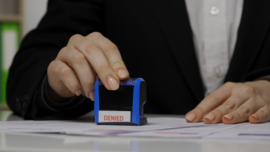 Shot of female worker puts stamp with denied mark written on it