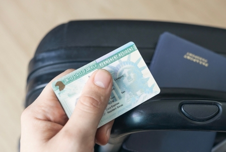 Man holding permanent resident (green) card. United States passport   on suitcase. Application to register permanent residence.